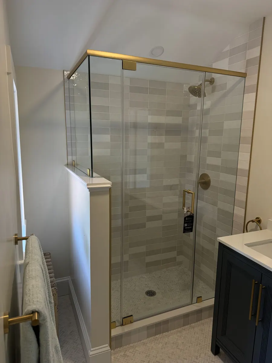 Frameless glass shower with satin brass hardware, installed by IDEAL Shower Doors