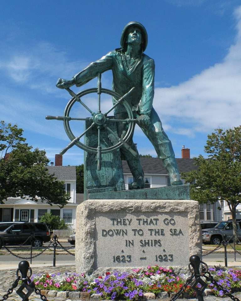 Bronze sailor statue steering ship’s wheel outdoors