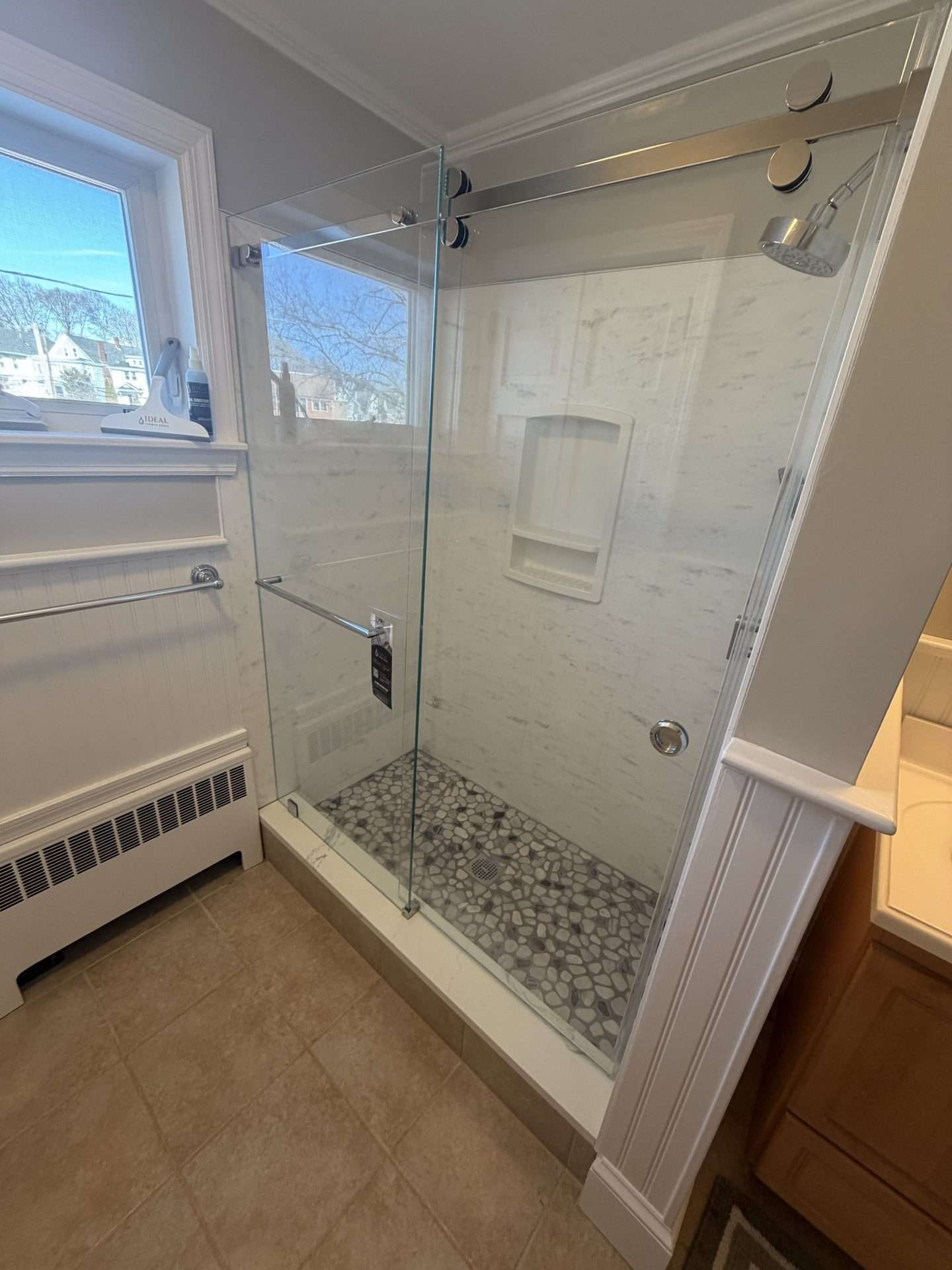 Sliding glass frameless shower door on marble-look tub enclosure with pebble stone floor, Milton MA
