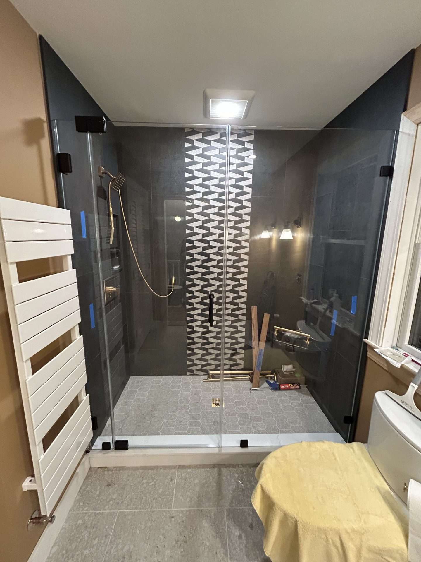 Dark charcoal large-format tile walk-in frameless shower with geometric accent strip and matte black hardware