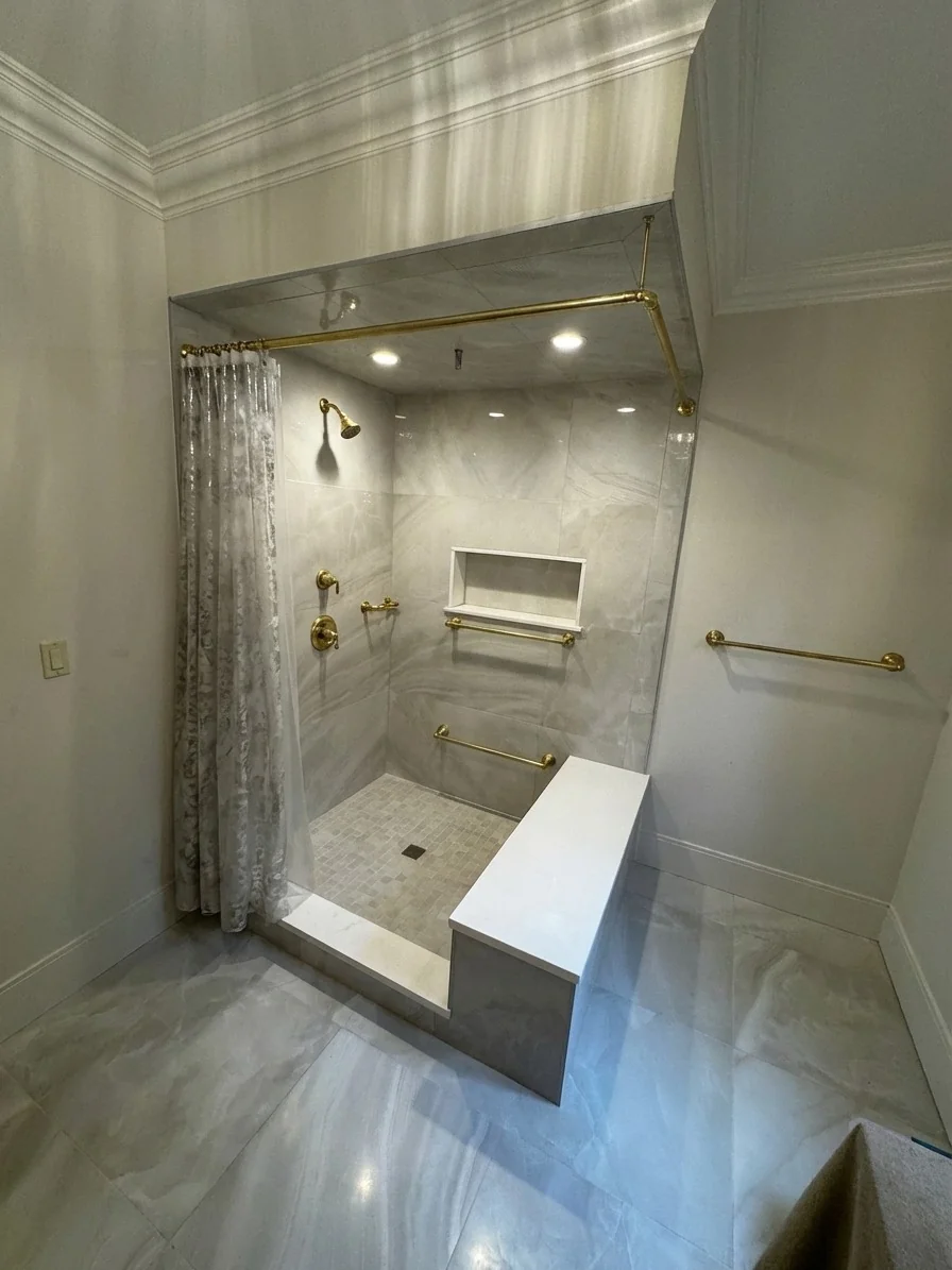 Custom shower with brushed gold curtain rod, recessed niche, built-in bench, and large-format marble tile in Rockport, MA