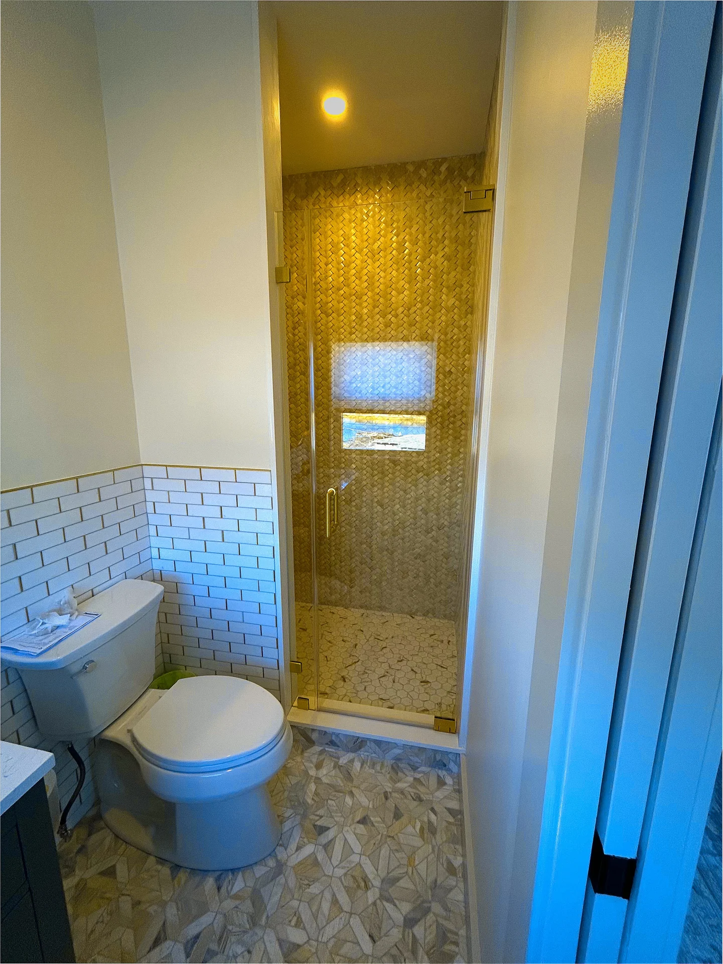 Frameless pivot shower door with brushed gold hardware and gold mosaic tile in Beverly MA