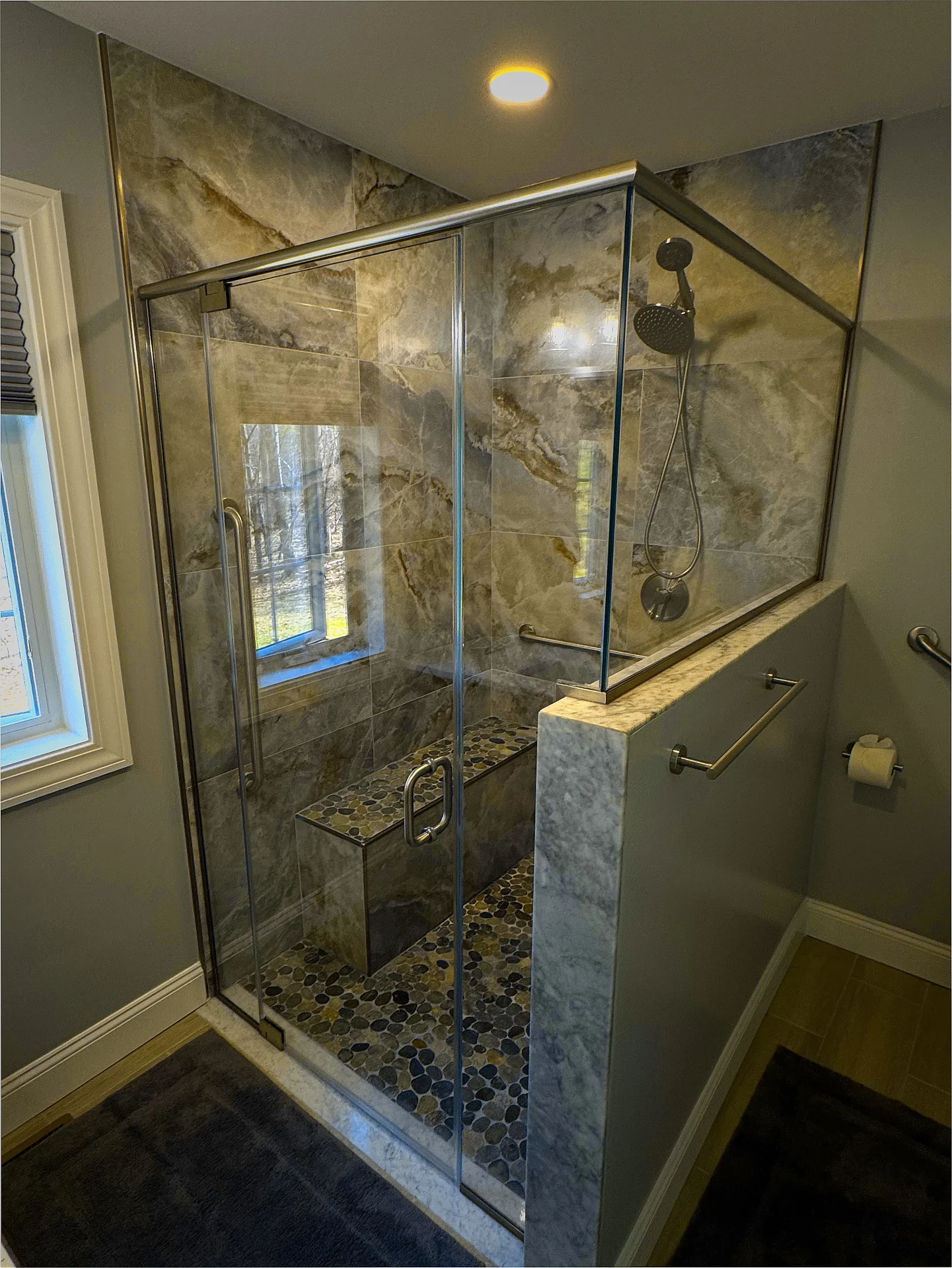 Frameless corner shower with marble slab walls and pebble-stone bench in Bow NH