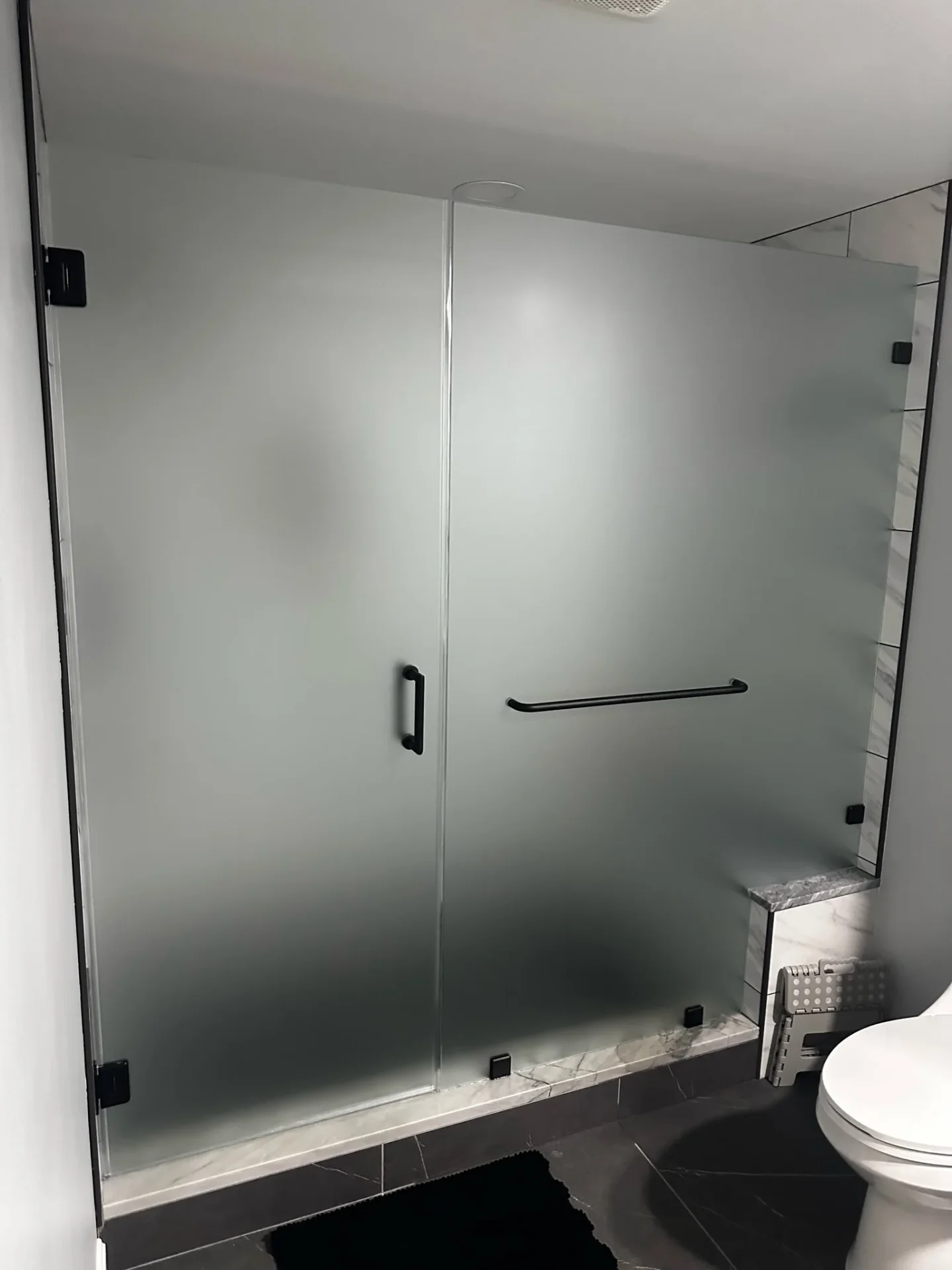 Frameless pivot shower door, matte black hardware, marble tile, Dedham MA