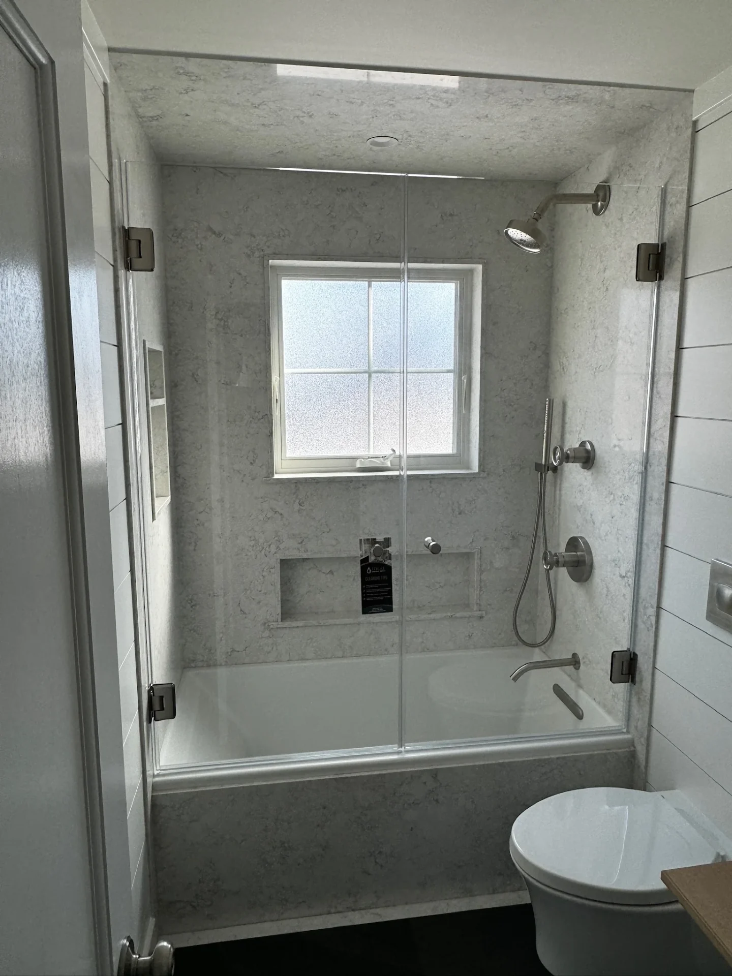 Frameless hinged shower door, brushed nickel hardware, marble-look walls, Beverly MA