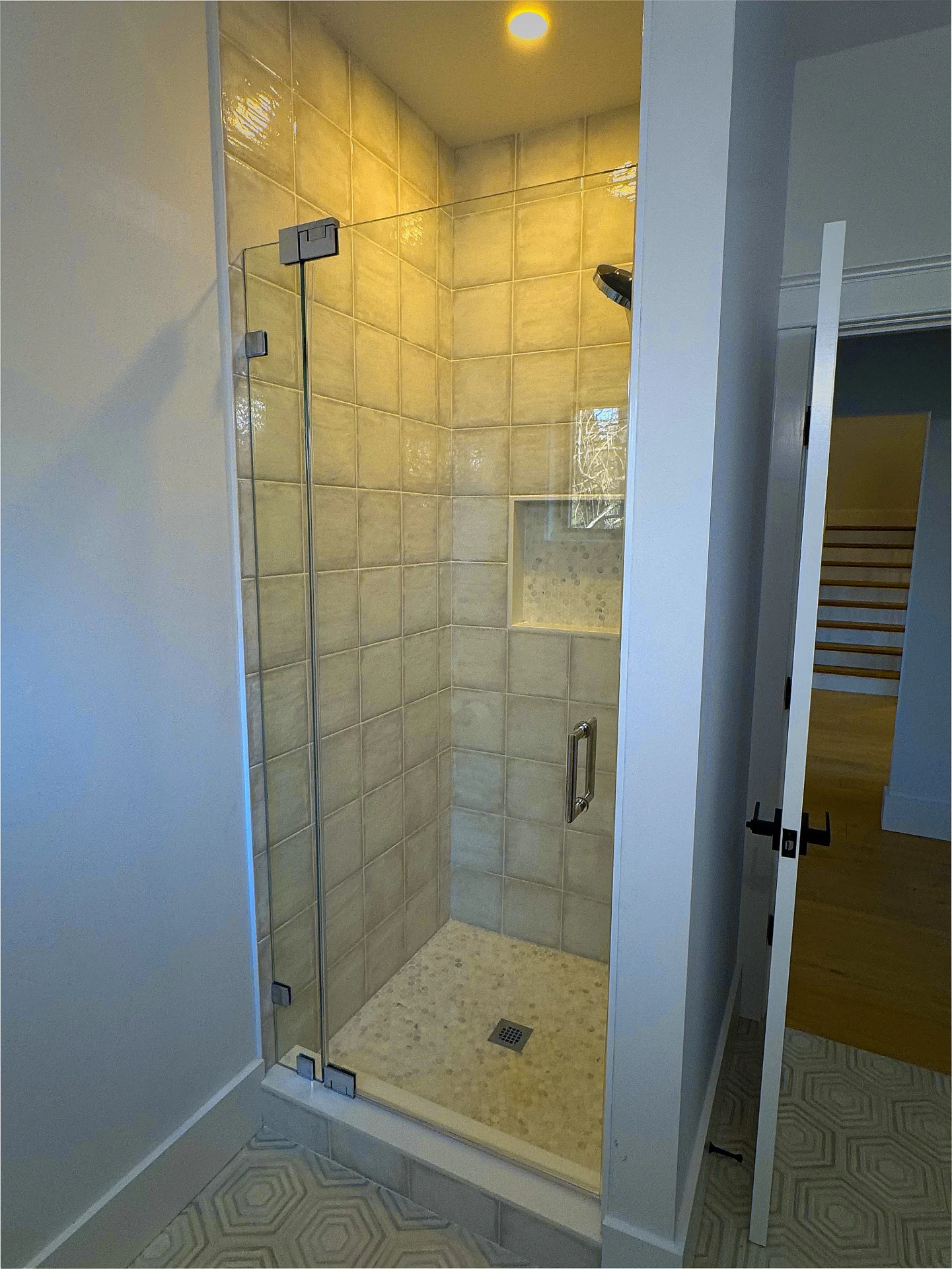 Frameless pivot door, matte black hinges, glossy subway tile, Natick MA