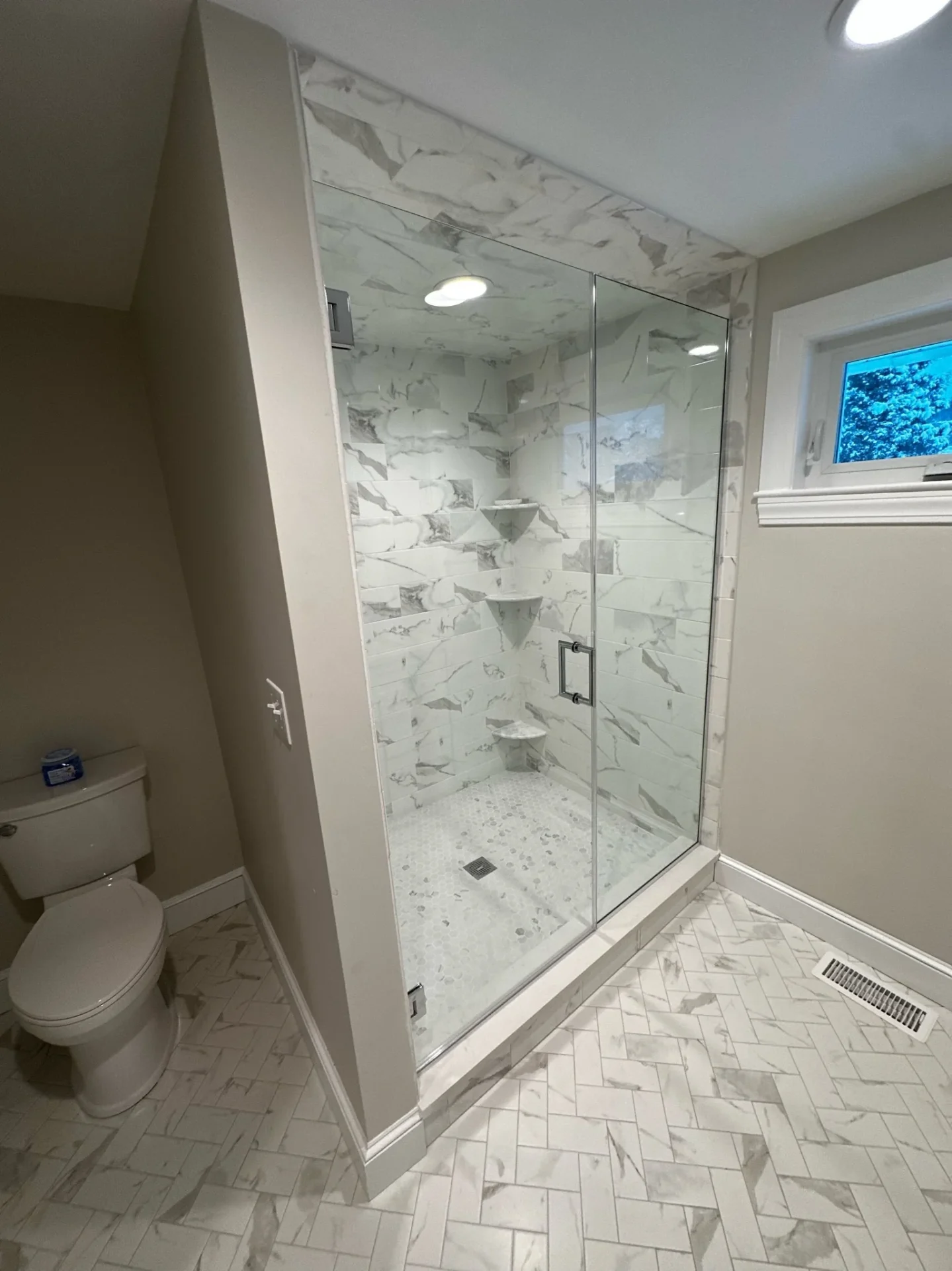 Frameless hinged shower door with marble herringbone floor in Newburyport MA