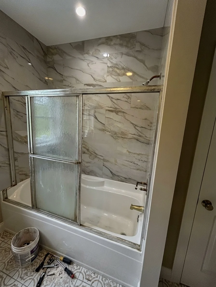 Corroded framed sliding tub door with fogged glass before frameless replacement in Malden, MA bathroom