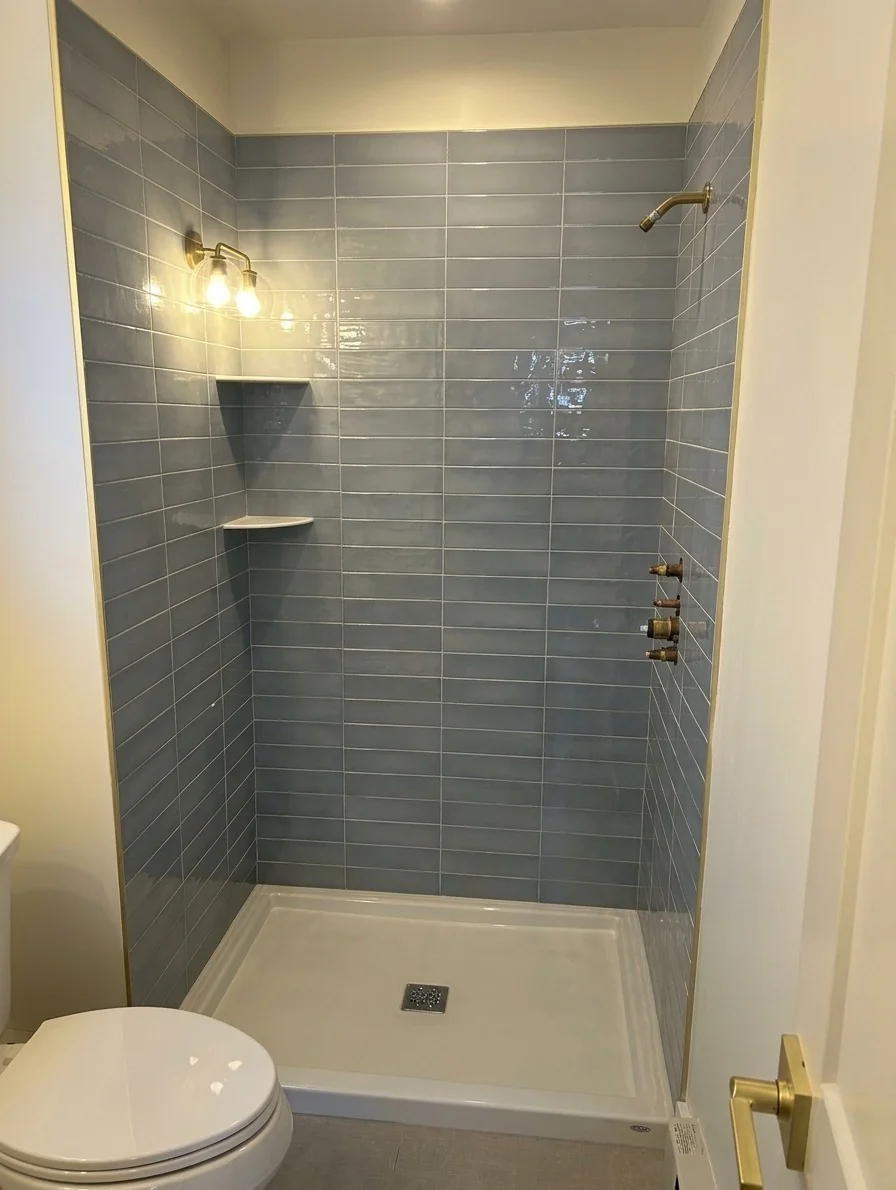 Brass-framed hinged shower door over blue subway tile in a Salisbury, MA bathroom