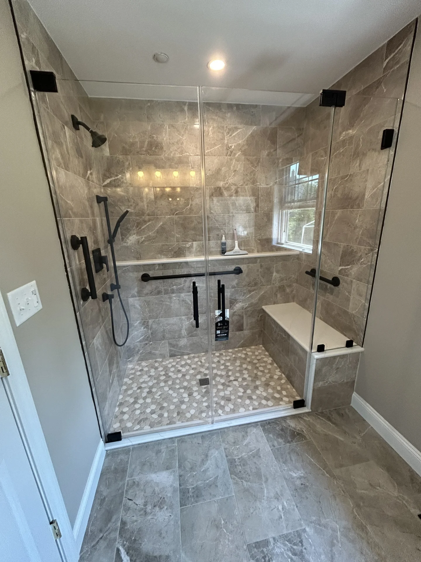Frameless shower door with matte black grab bars, marble tile, Haverhill MA