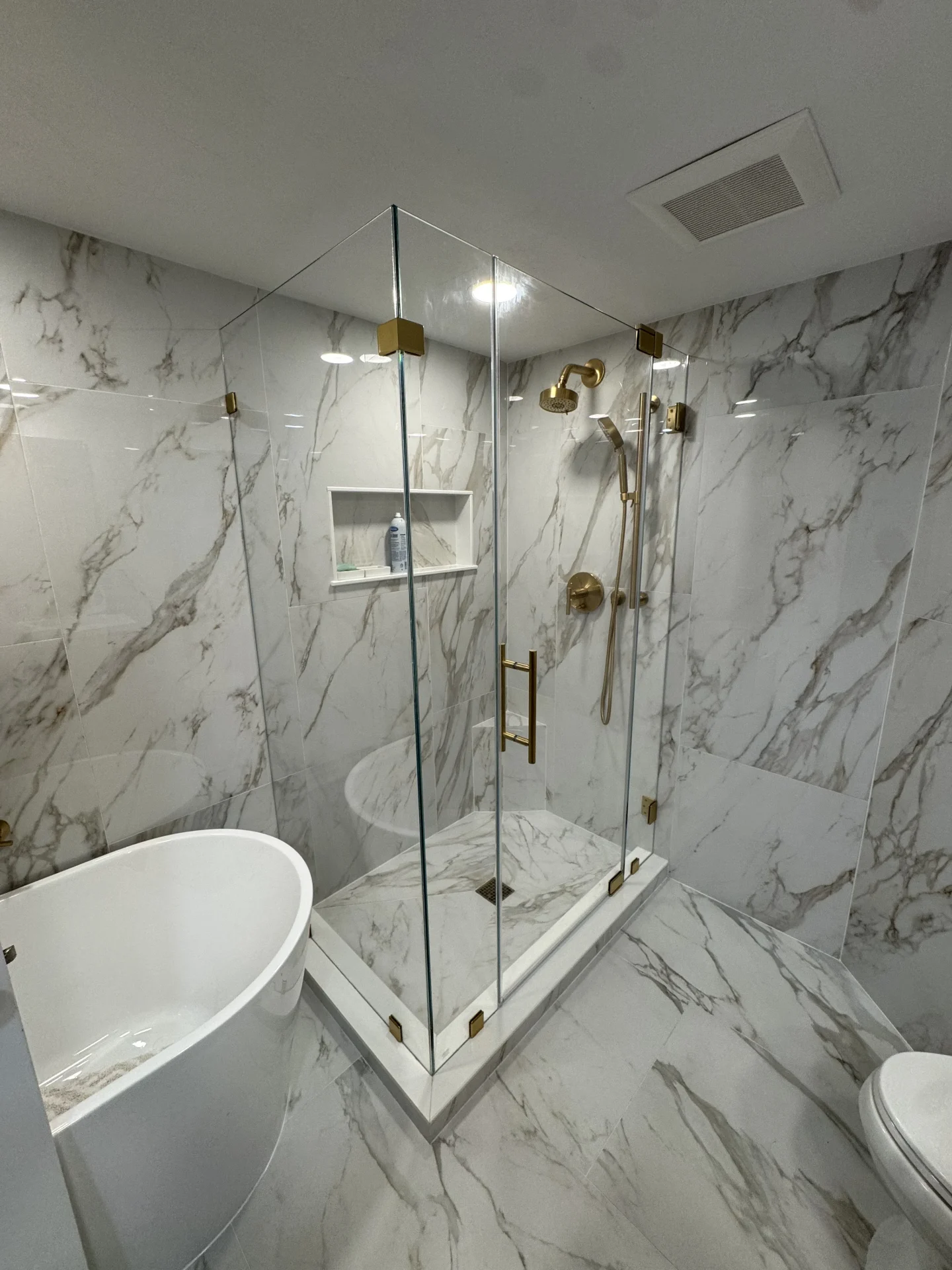 Frameless corner shower enclosure with brushed brass hardware and marble tile in Manchester-by-the-Sea MA