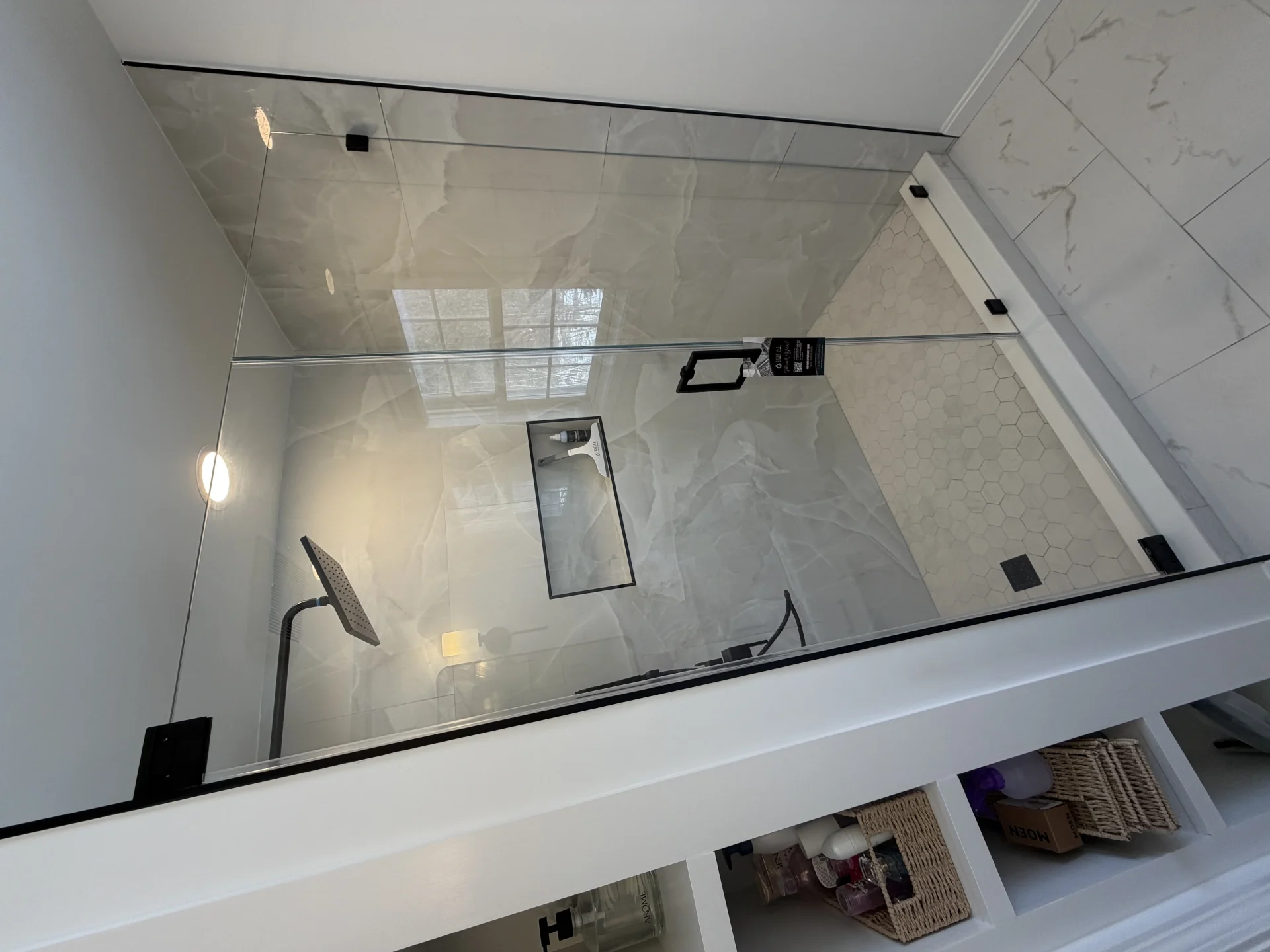 Frameless shower door with matte black hardware and marble hexagon tile, Needham