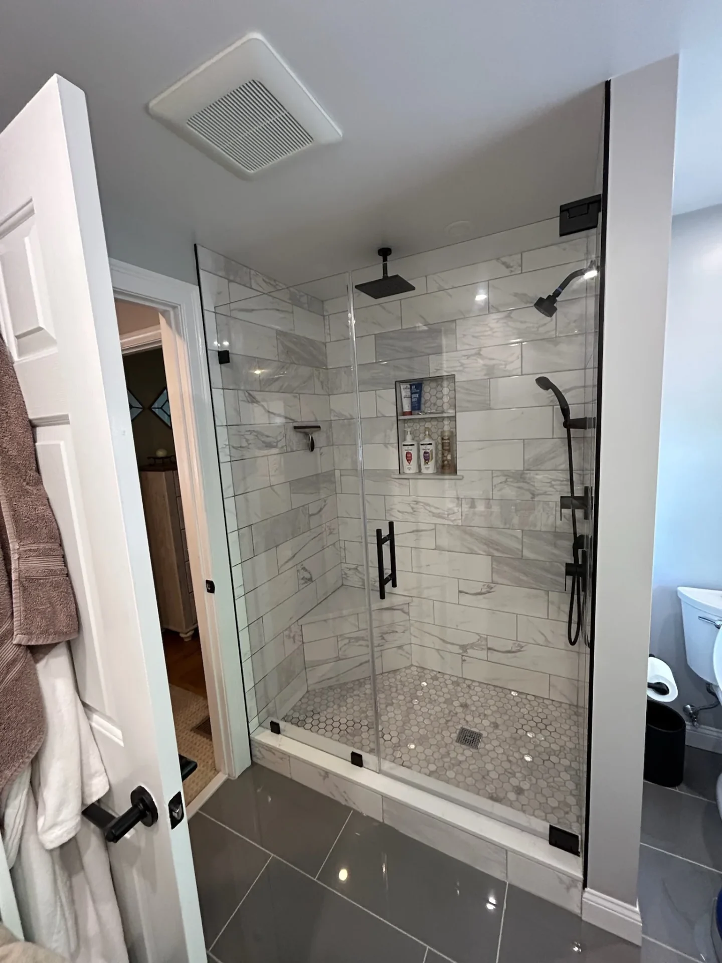 Frameless pivot shower door, matte black hardware, marble tile bench, Salem MA